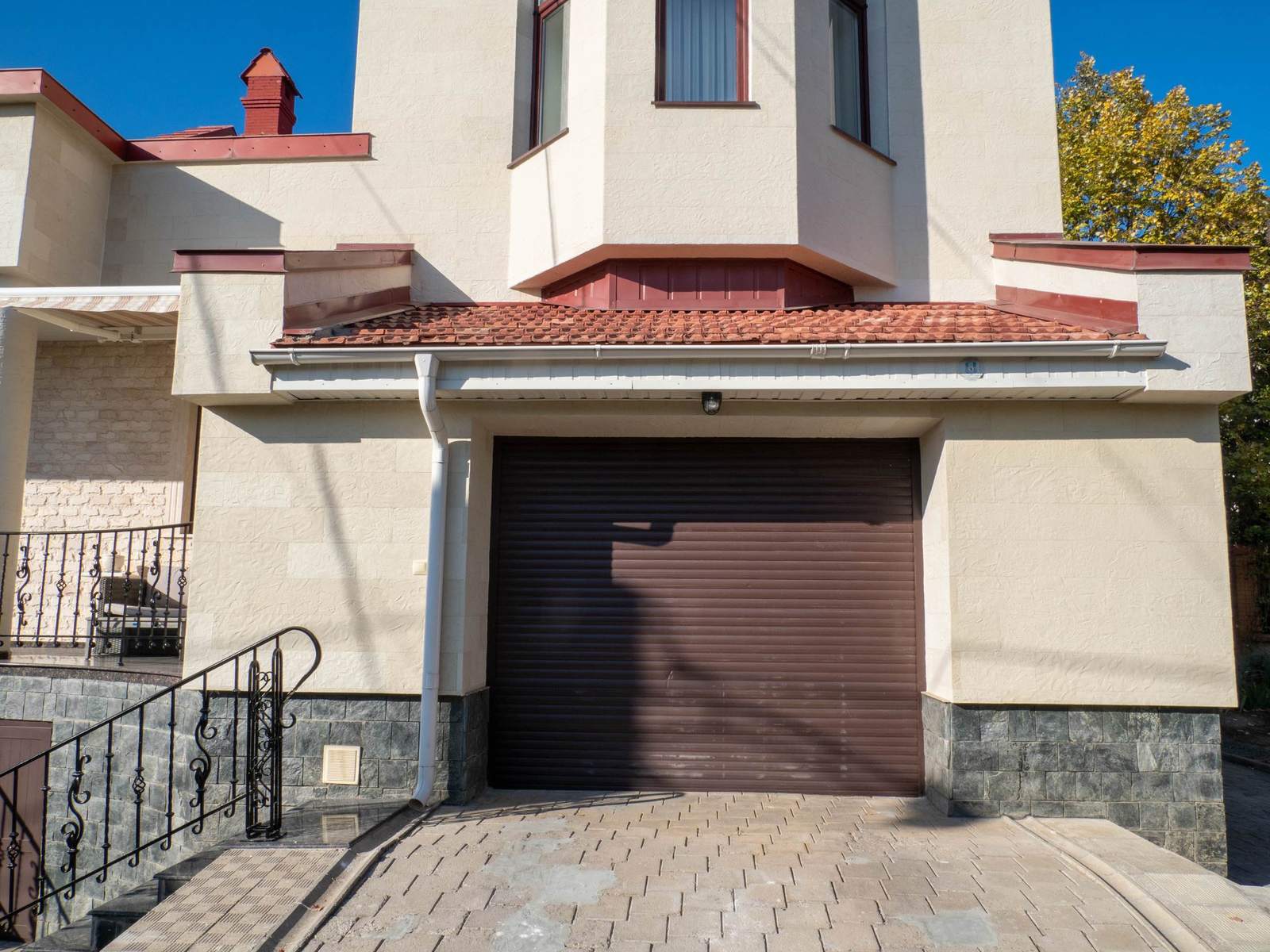 Ușă de garaj maro sub fronton, fațadă din piatră flexibilă Tender Rock și alee pavată